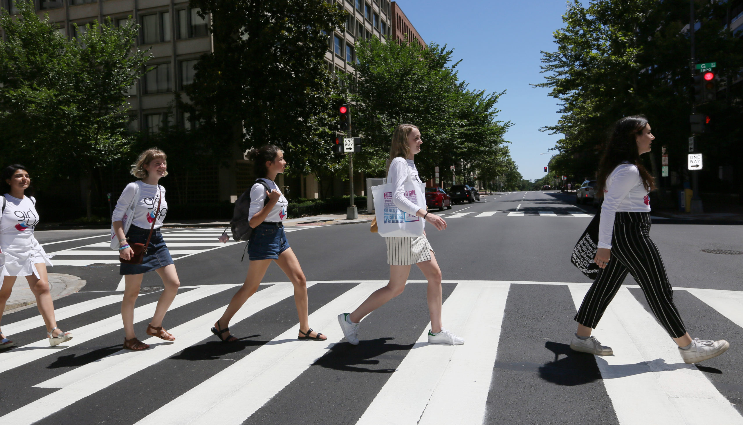 5 girls cross street one after other facing forward with their teen adviser shirt on